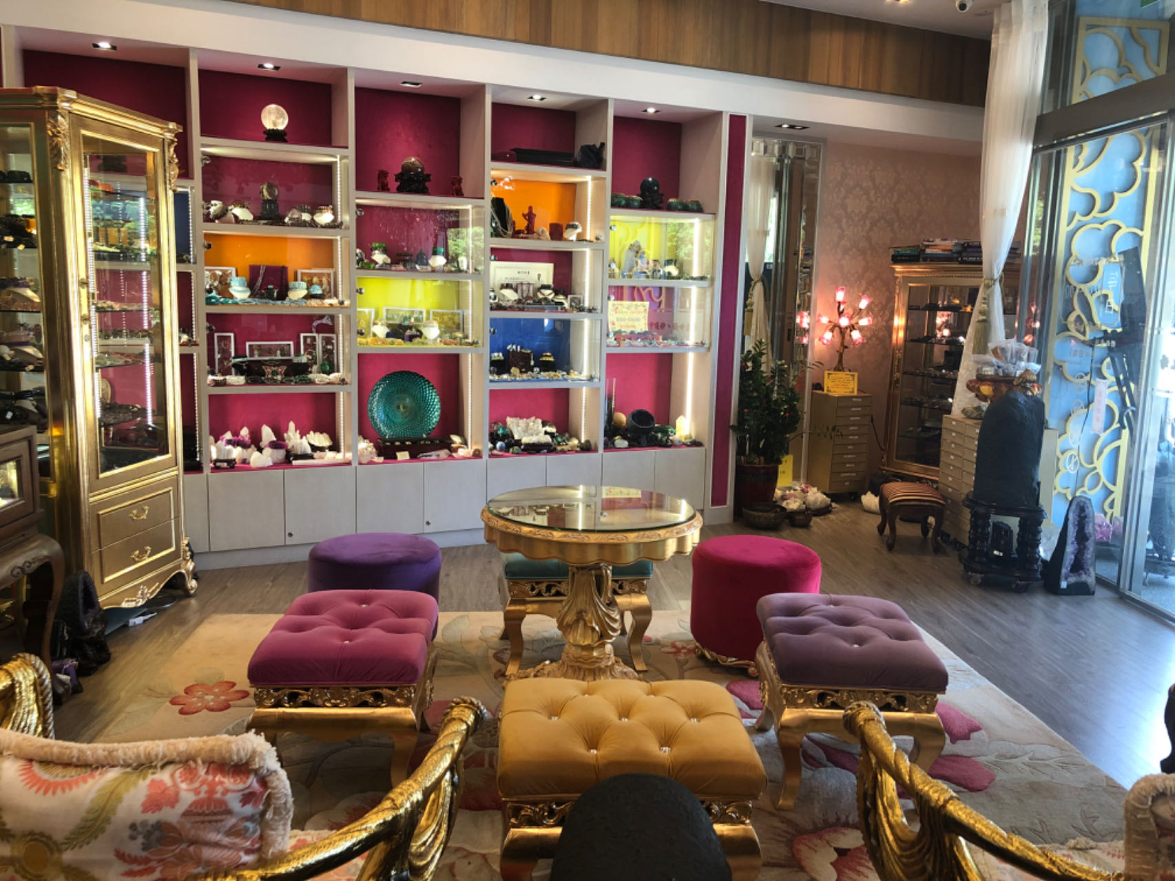 台北門市店內：桃紅色展示牆陳列各式水晶，前方是金色雕花圓桌與絲絨坐凳